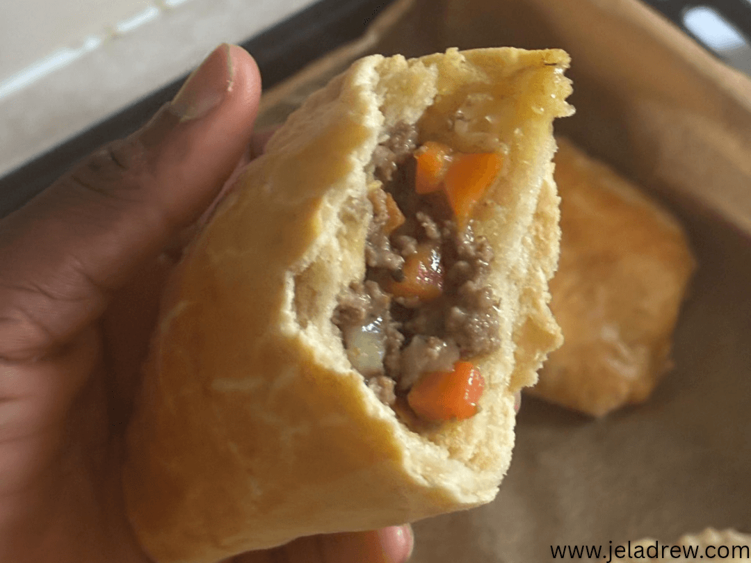 A-close-up-of-a-freshly-baked-Nigerian-meat pie-with-a-flaky-golden-crust-filled-with-minced-meat-carrots-and-potatoes-held-in-hand
