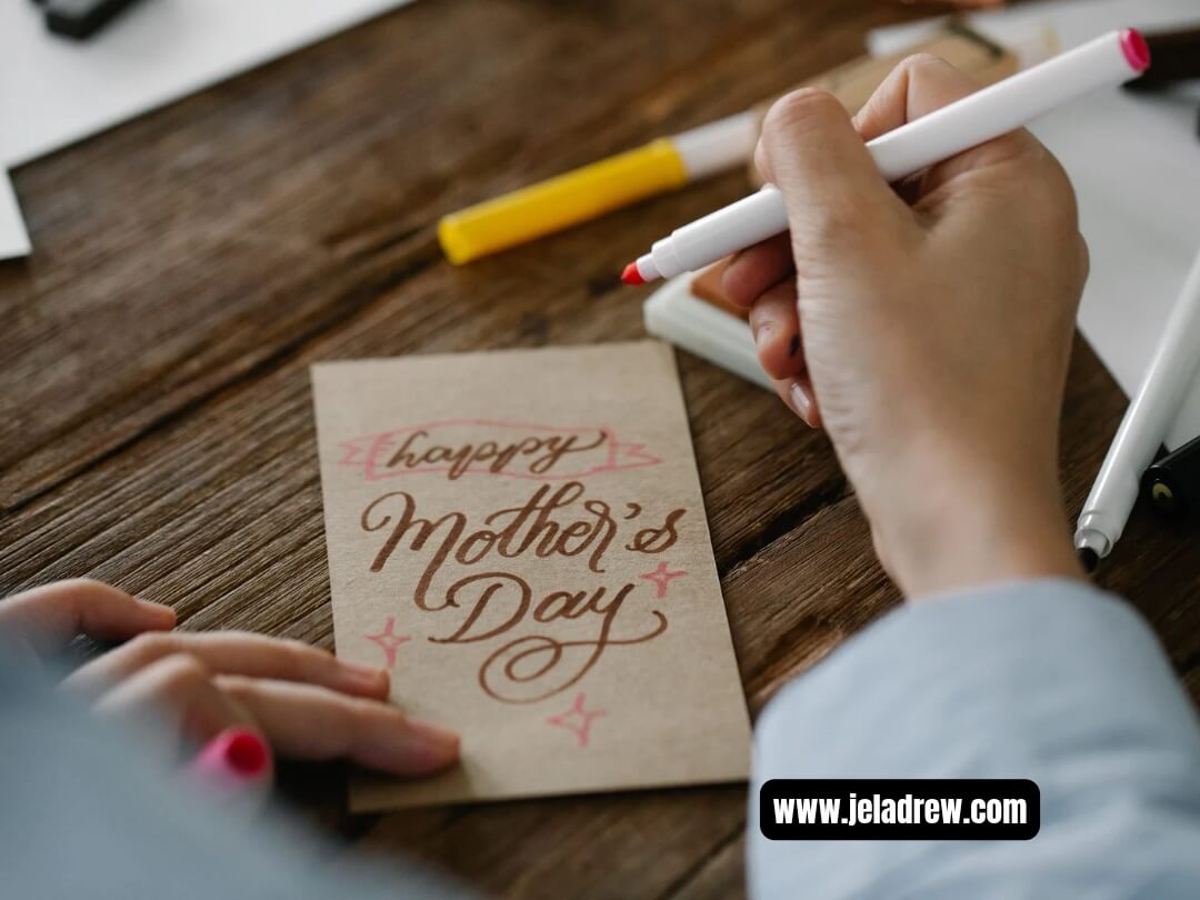 Hand-writing-a-hand-made-Mothers-Day-card-on-a-wooden-table-with-pens-and-stationery